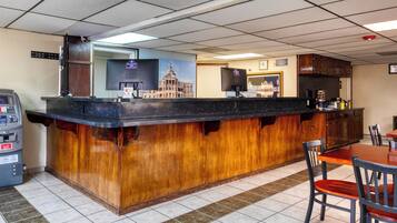 A bar area with a wooden counter, a cash register, a coffee machine, and a seating area with chairs and a table.