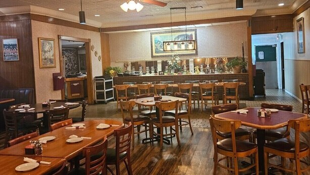 Un ristorante con tavoli e sedie in legno, un'area bar e un soffitto con motivo decorativo.