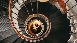 A spiral staircase with a central light fixture and a chain-link railing. - Château d'Ouchy (Lausanne)
