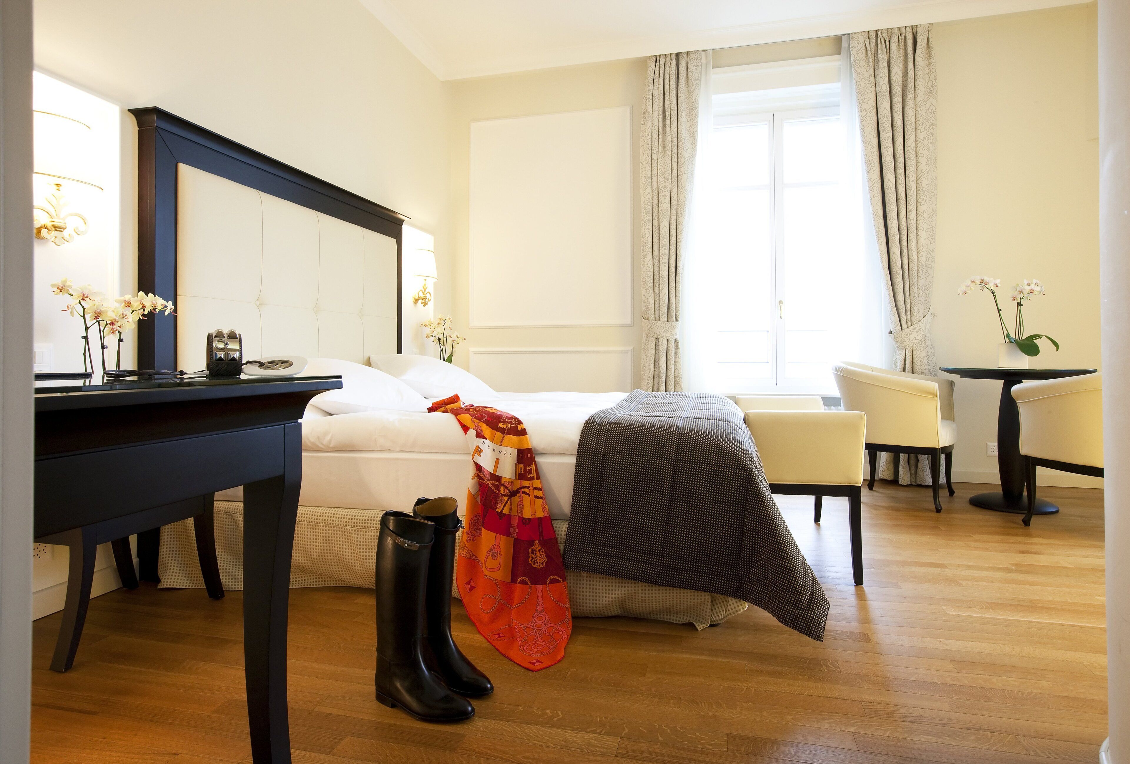 Ein Hotelzimmer mit einem Bett, einem Schreibtisch, einem Sessel und einem Tisch mit Blumen in einer Vase.
