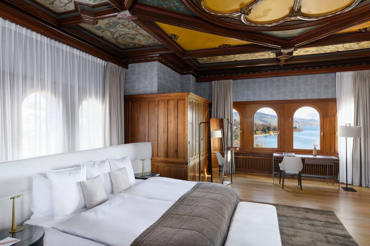A spacious bedroom with a large bed, a desk, and a view of the sea through arched windows.