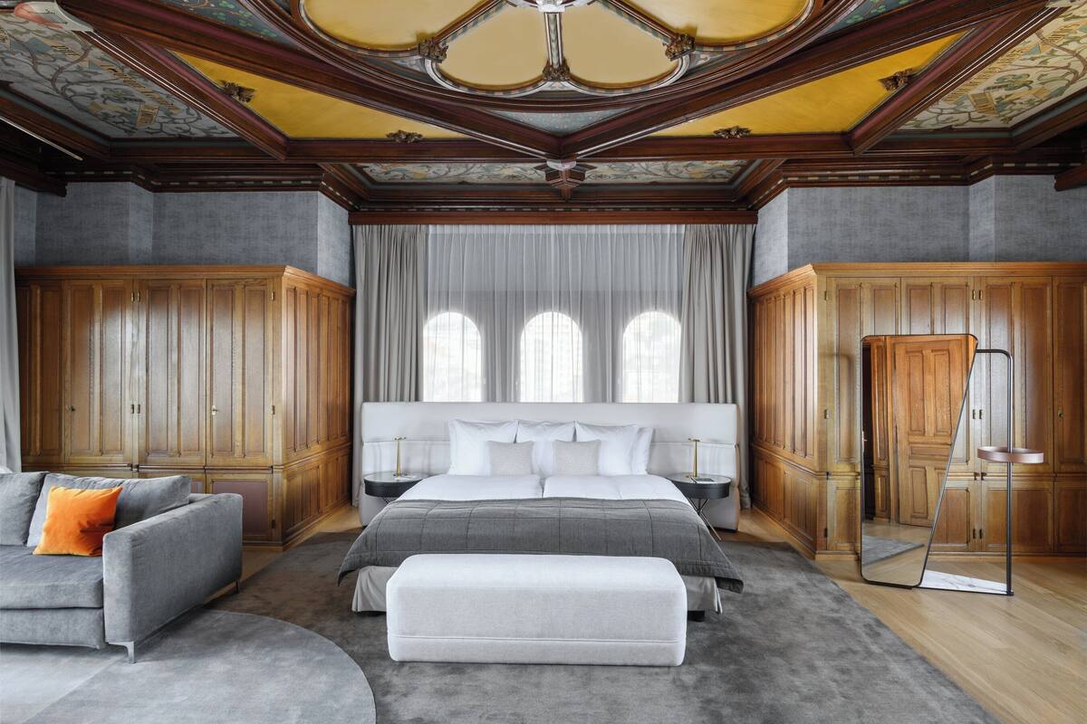 A spacious bedroom with a large bed, a grey sofa, and a wooden wardrobe.