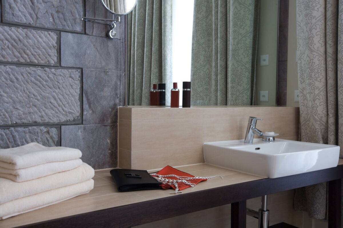 A bathroom with a stone wall, a sink, a mirror, and a window with patterned curtains.