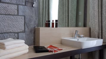 Un baño con pared de piedra, un lavabo, un espejo y una ventana con cortinas estampadas.