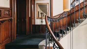 Un escalier en bois, agrémenté de rampes en métal ouvragé et surmonté d’un palier recouvert d’une moquette noire.