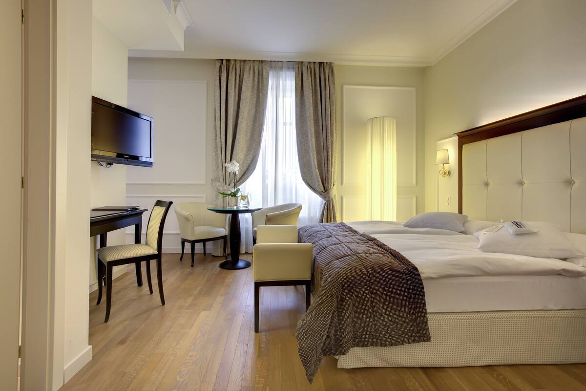 A hotel room with a bed, a desk, a chair, a TV, and a window with curtains.