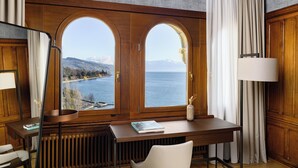 A room with a wooden desk, a view of a lake, and a lamp. - Château d'Ouchy (Lausanne)