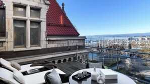 A terrace with a view of a marina and harbor, furnished with lounge chairs and a table with a tray of items. - Château d'Ouchy (Lausanne)