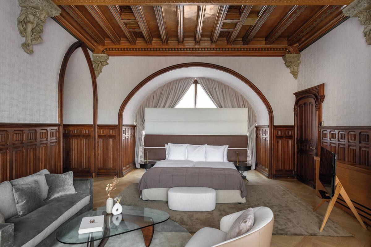 A spacious bedroom with a large bed, a sofa, a glass coffee table, and a TV stand.