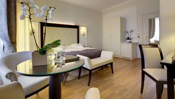 A modern hotel room with a bed, a sitting area with a glass table, a chair, and a desk.