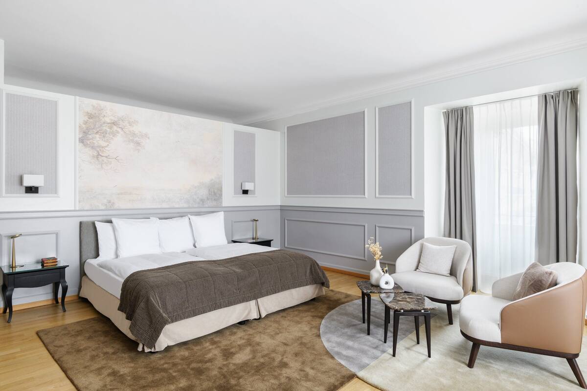 A modern bedroom with a large bed, bedside tables, a chair, and a view of the outdoors.