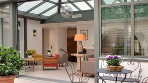 A spacious indoor area with a glass ceiling, wicker furniture, and potted plants. - Hôtel Le Littré (Paris)