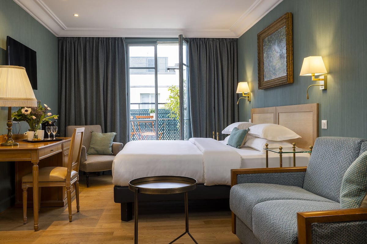 Una habitación de hotel con una cama, un escritorio con lámpara, una silla y una mesita.