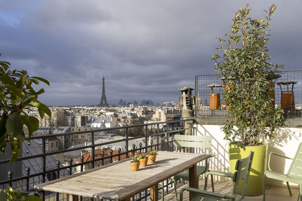 Una terraza en la azotea con vistas a la Torre Eiffel, plantas en macetas y una mesa de madera.