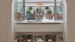 A spacious lobby with a high ceiling, a central staircase, and a view of a terrace with outdoor seating and potted plants. - Hôtel Le Littré (Paris)