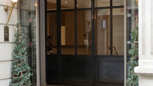 A hotel entrance with a large glass door, a small potted plant, and a wall-mounted light fixture. - Hôtel Le Littré (Paris)