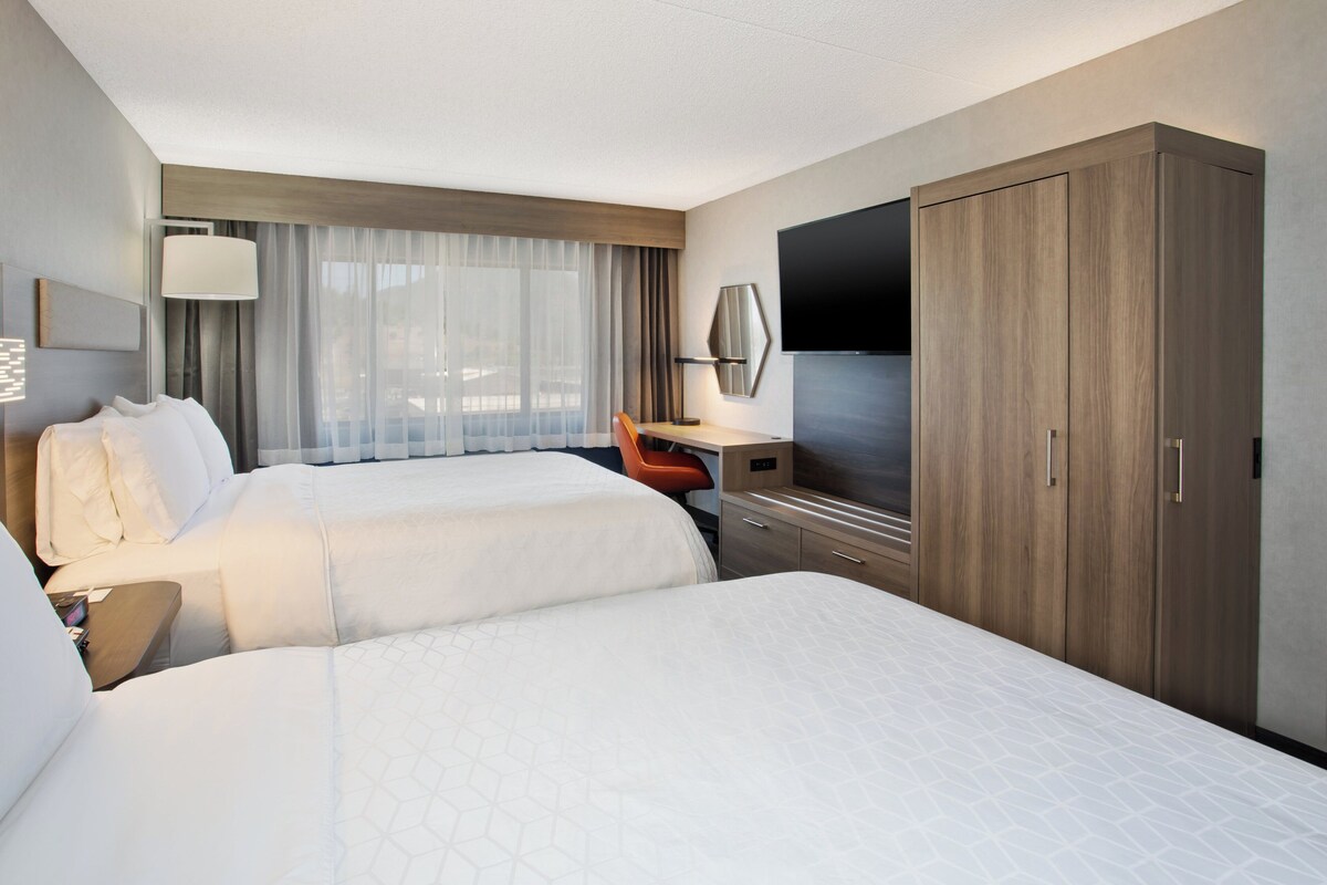 A hotel room with two beds, a desk with a chair, a TV, and a wardrobe.