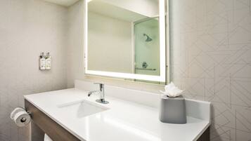 A modern bathroom with a white sink, a large mirror, and a glass shower enclosure.