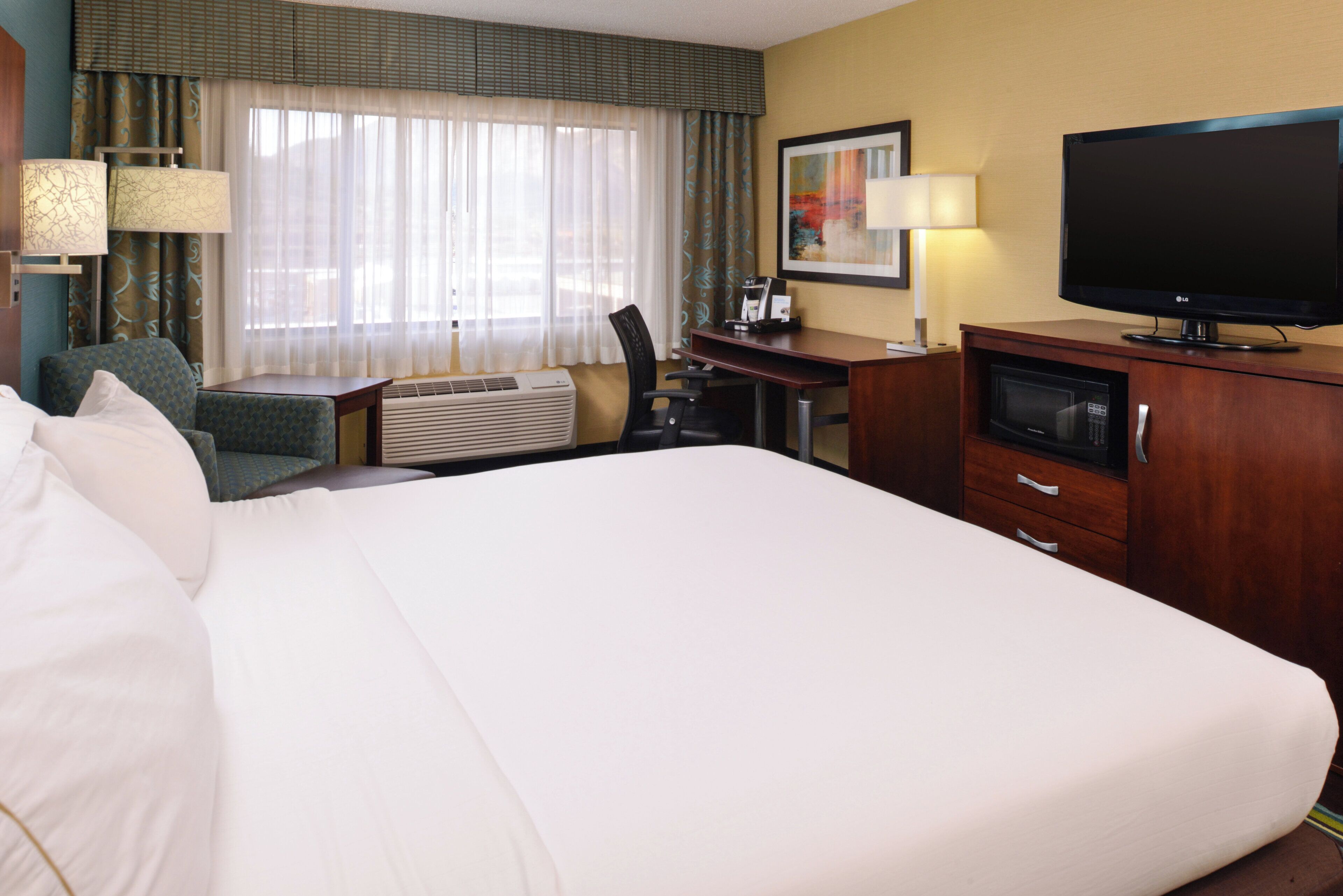 A hotel room with a large bed, a desk, a television, and a coffee machine.