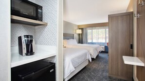 A hotel room with a kitchenette, a bed with white bedding, a bedside table, a wardrobe, and a window with curtains. - Holiday Inn Express Flagstaff by IHG (Flagstaff)