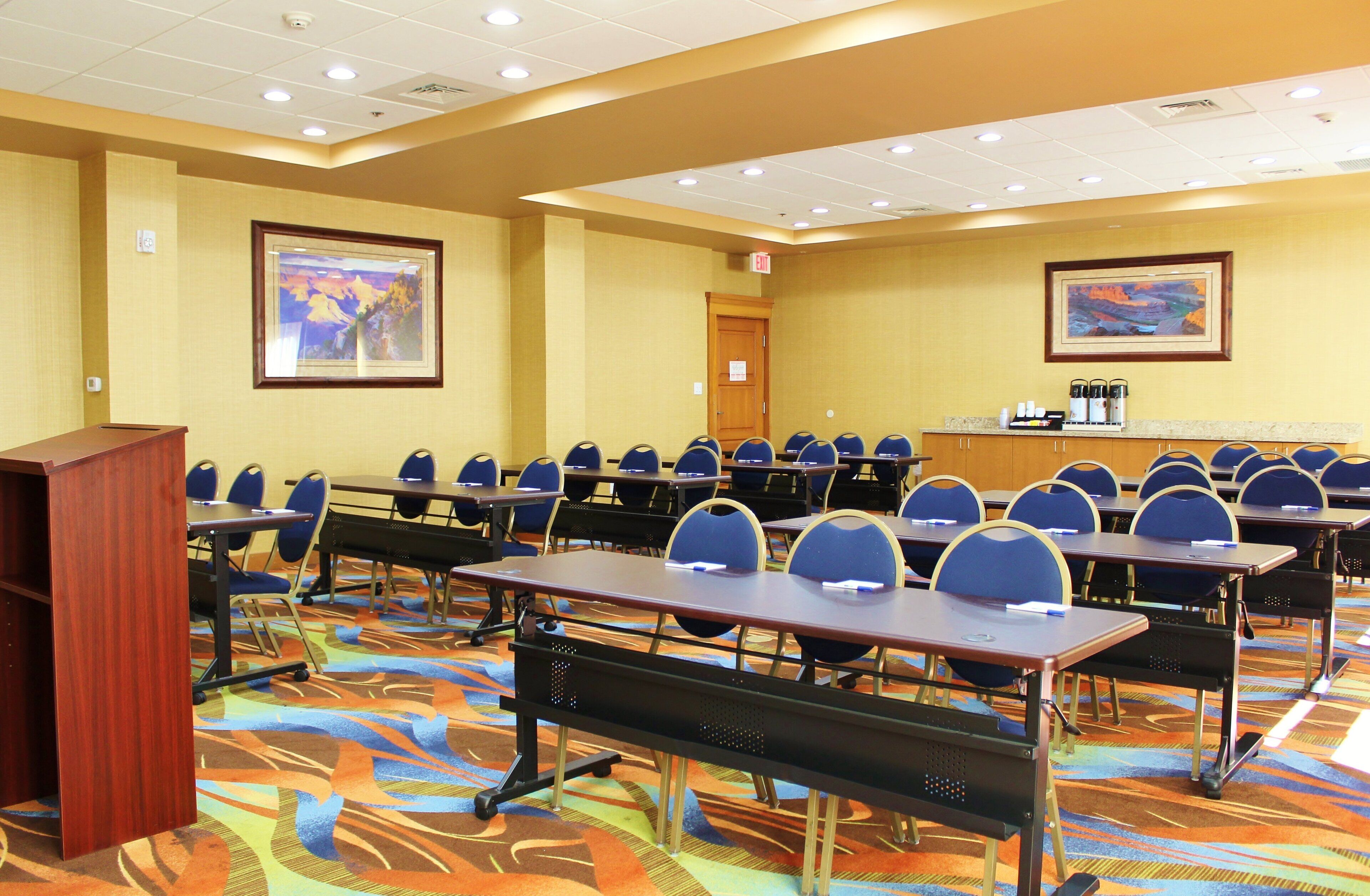 A conference room with rows of tables and chairs, a podium, and framed artwork on the walls.