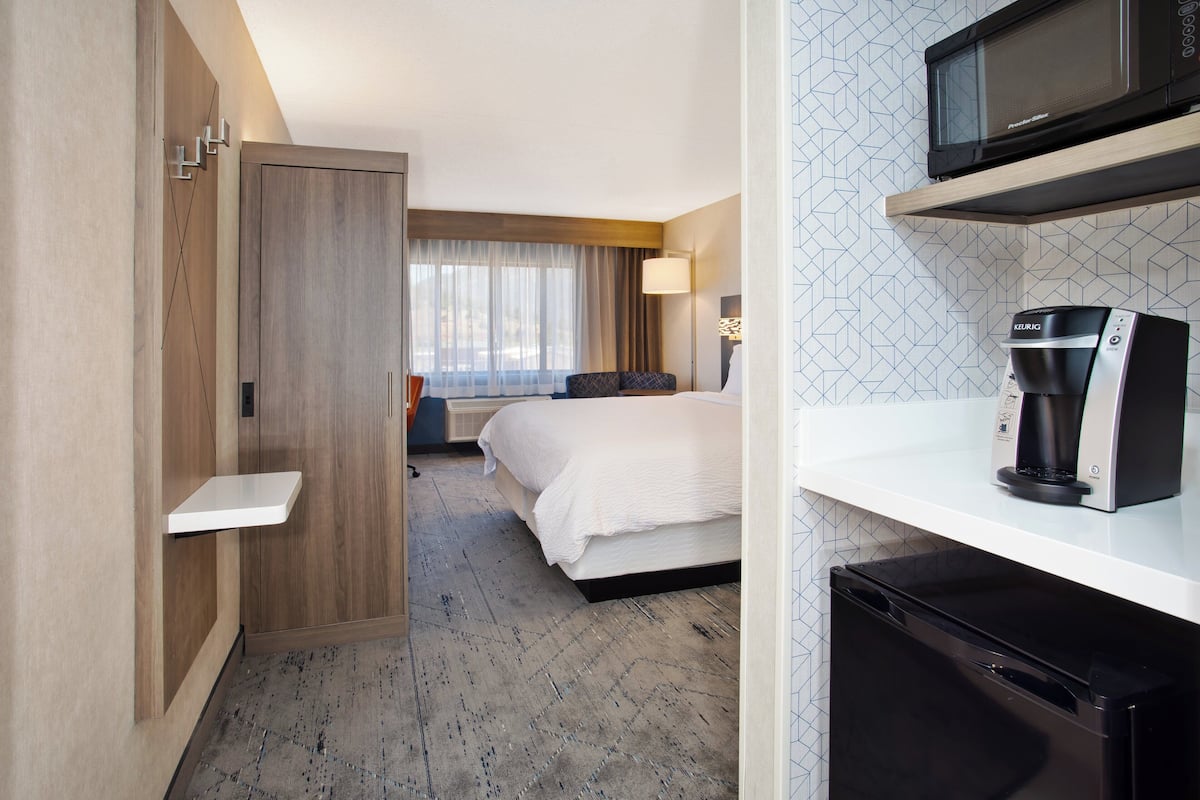 A hotel room with a bed, a microwave, a coffee maker, and a small sink.