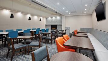 A conference room with multiple tables and chairs, a fireplace, and a television mounted on the wall.