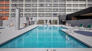 Una piscina con sillones de descanso y un edificio de hotel al fondo.