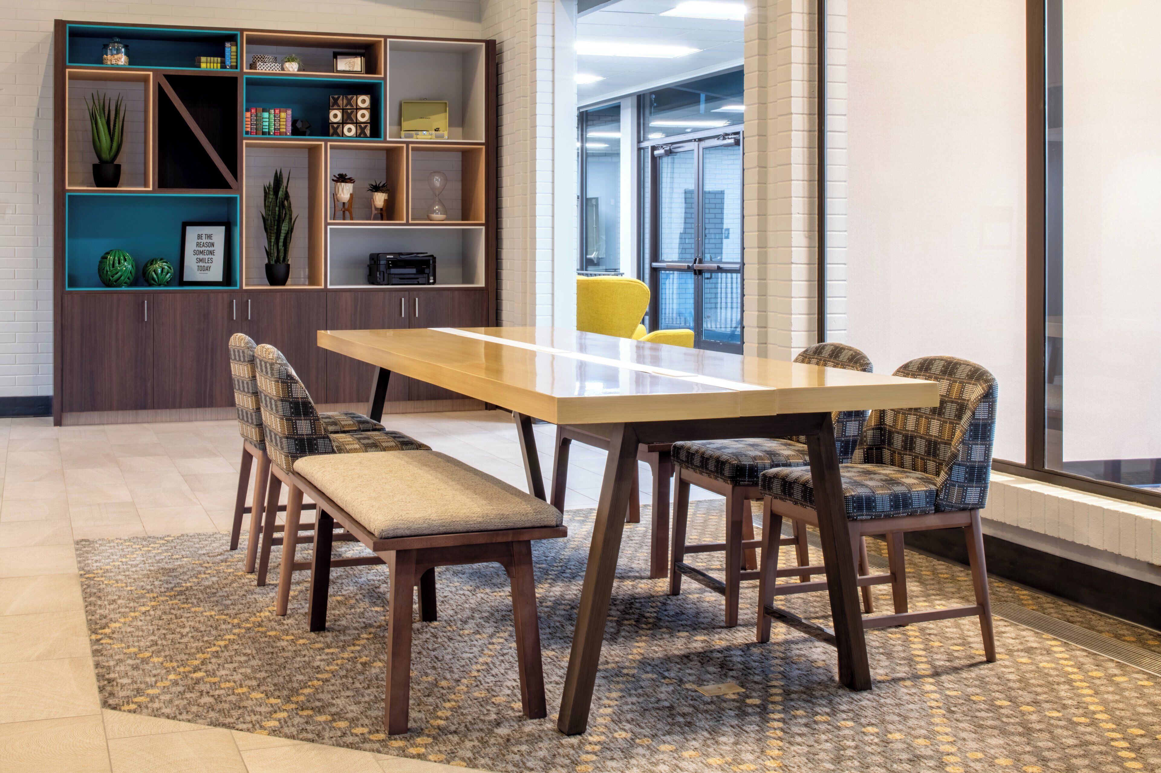 A conference room with a long table, four chairs, a bookshelf, and a potted plant.
