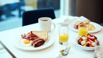 Mesa de café da manhã com pratos de comida, uma xícara de café e um copo de suco de laranja.