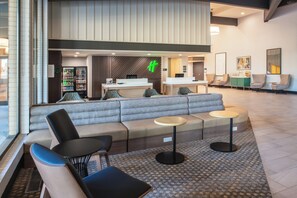 Um lobby de hotel moderno com área de estar, balcão de recepção e bar de lanches.