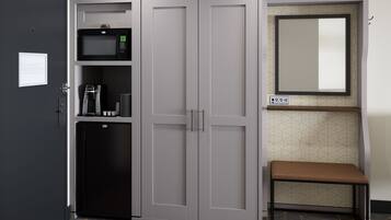 A room with a wardrobe, a microwave, a coffee machine, and a small bench.