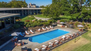 A swimming pool with sun loungers and tables, surrounded by a fence, with a building and trees in the background. - Holiday Inn Richland on the River by IHG (Richland)