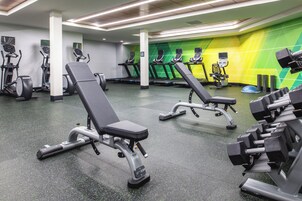Un gimnasio con equipos de ejercicio variados, incluyendo cintas de correr, elípticas y bancos de pesas.