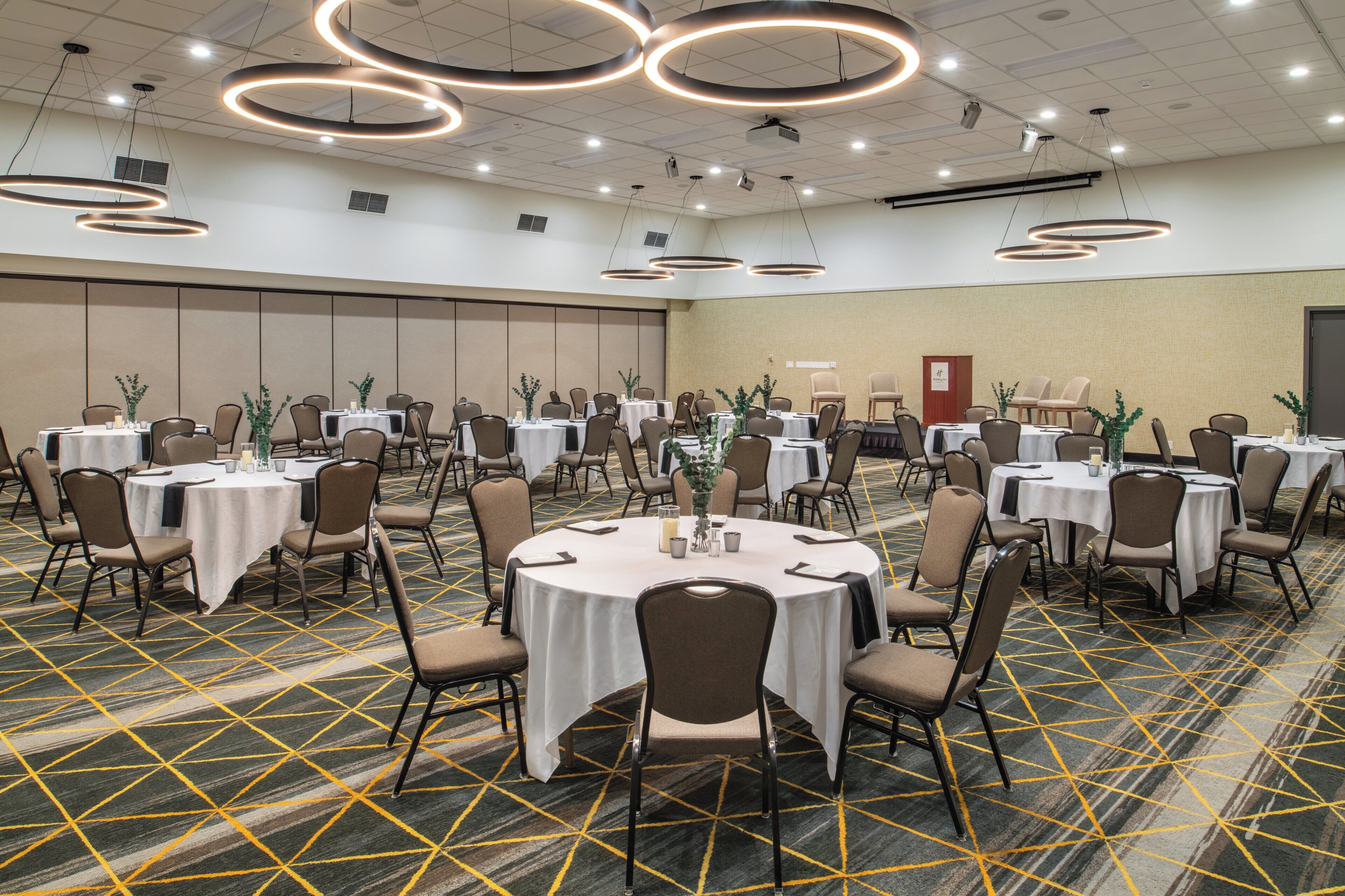A conference room with multiple round tables, chairs, and a carpeted floor with a geometric pattern.