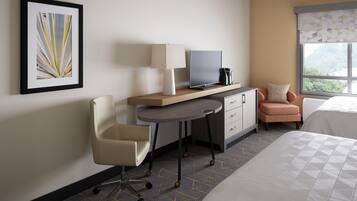 A hotel room with a bed, a desk with a chair, a TV, and a window with a view.