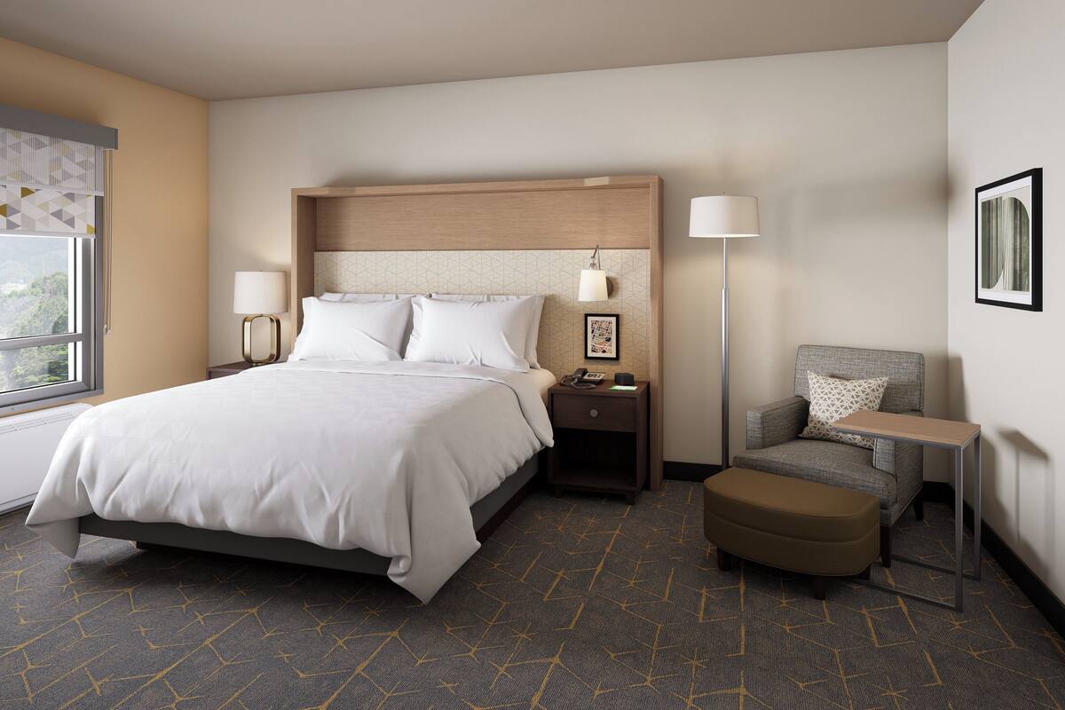 Ein Hotelzimmer mit Bett, Nachttischen, einem Sessel und einem kleinen Tisch.