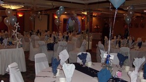 Un salón de banquetes con mesas redondas dispuestas para un evento formal, con manteles blancos, servilletas azules y decoraciones con forma de estrella.