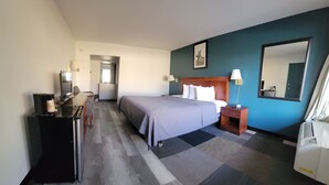 Habitación de hotel con cama, mesita de noche, escritorio con computadora y espejo.