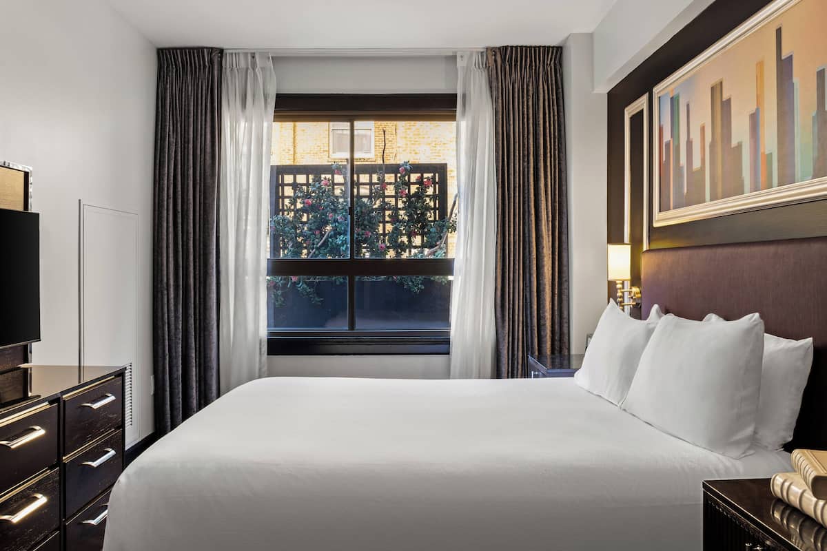 A hotel room with a large bed, a TV, a desk, and a window with curtains.