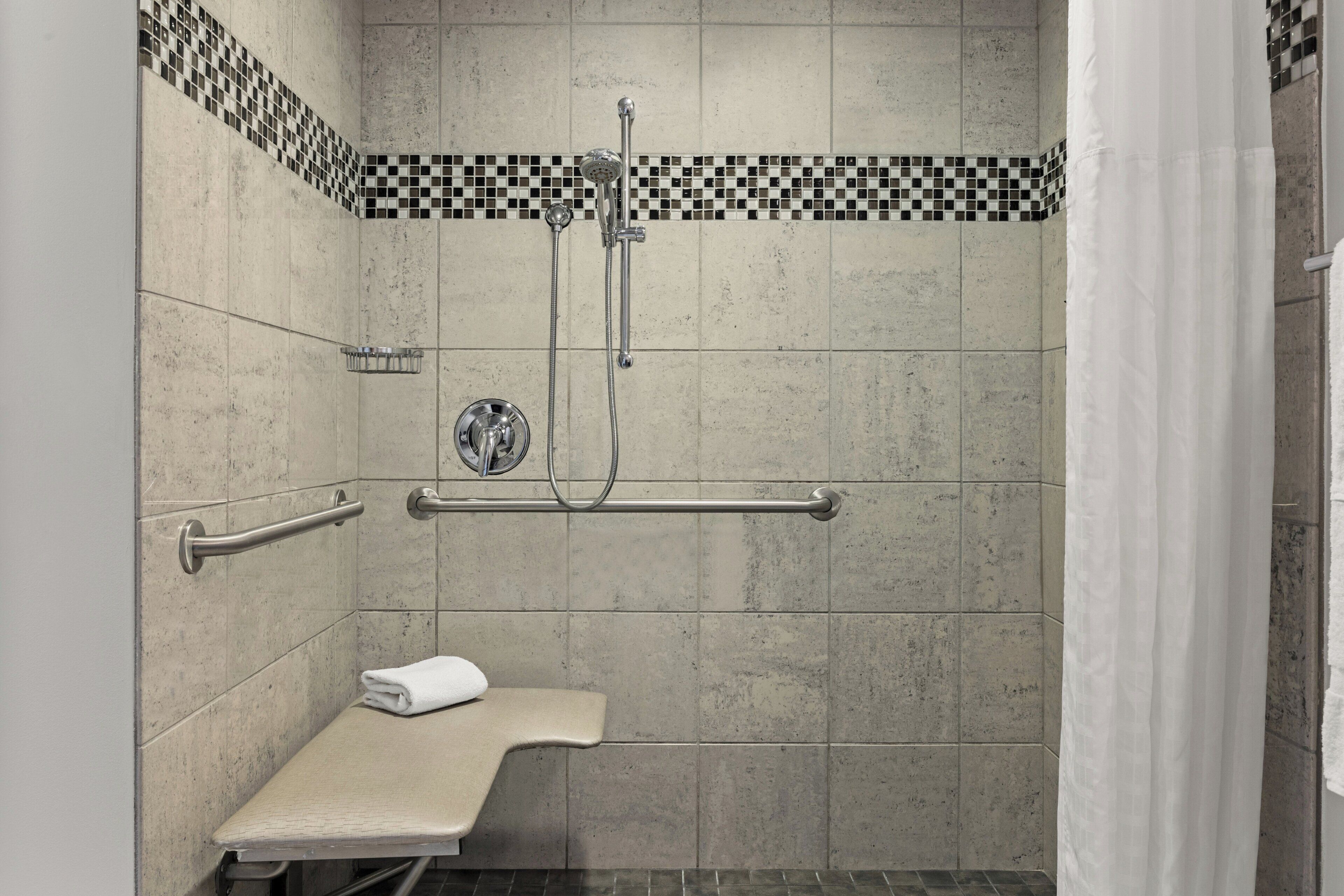 Un espace douche avec un mur carrelé, une barre d’appui, un pommeau de douche et un banc.