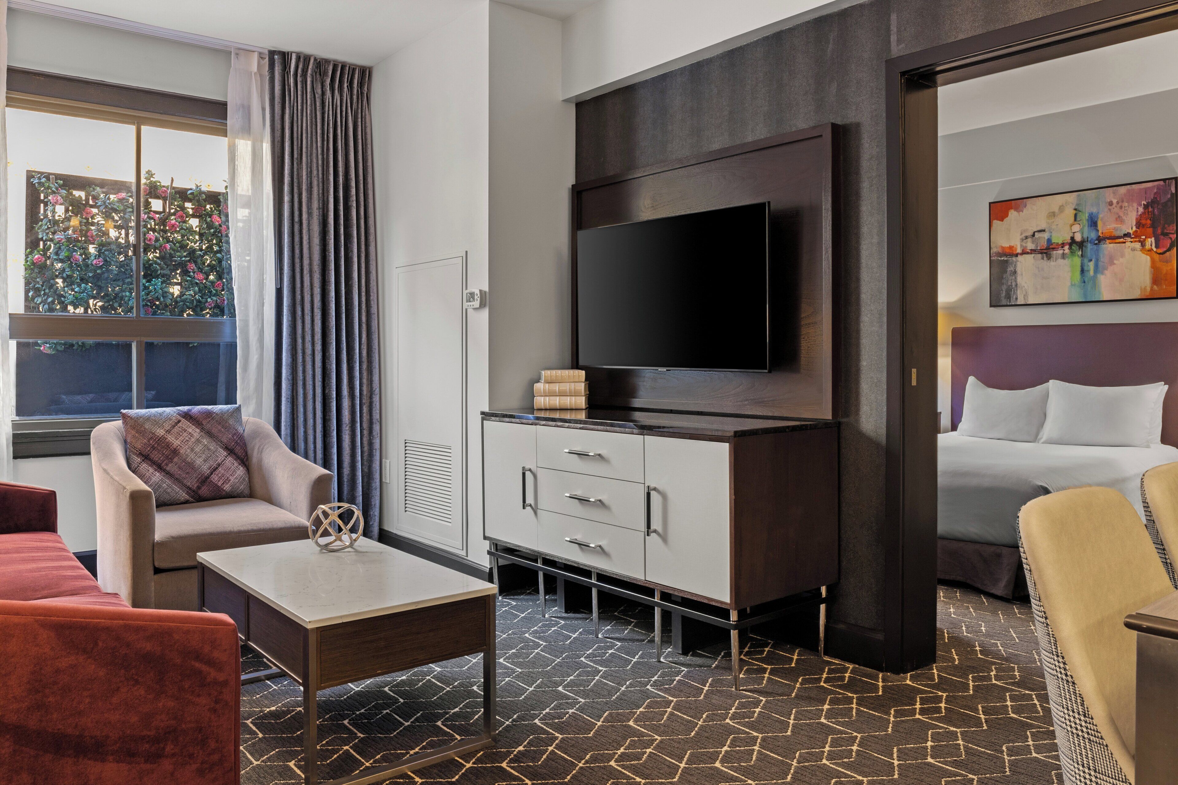 A hotel room with a flat-screen TV mounted on the wall, a sofa, a coffee table, and a bed with white bedding.