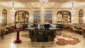 Een luxe hotel lobby met een bar in het midden, kroonluchters en een wijnrekken.