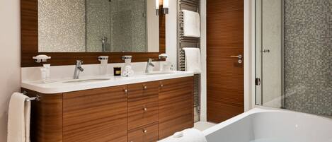 A modern bathroom with a large mirror, two sinks, a bathtub, and a shower area.