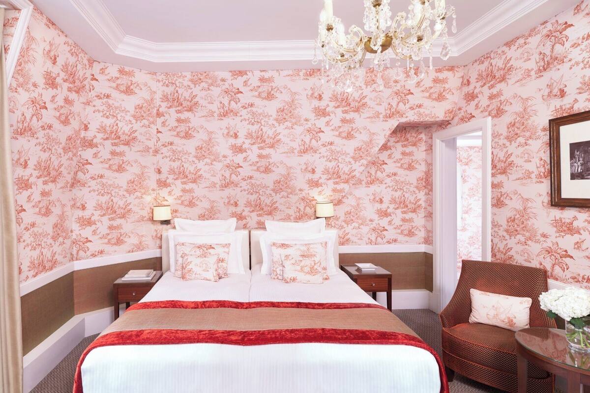A hotel room with a large bed, two bedside tables, a chair, and a chandelier.