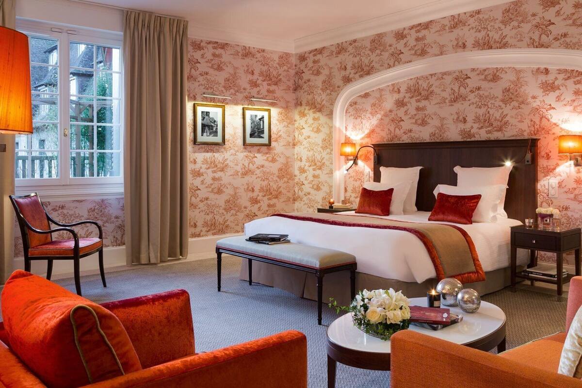 A hotel room with a large bed, two bedside lamps, a desk, a chair, and a window with curtains.