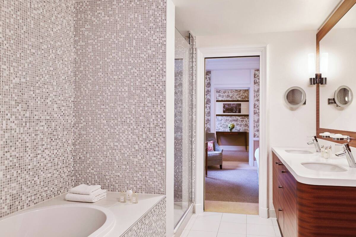 A modern bathroom with a mosaic tile wall, a large bathtub, and a vanity with a mirror.