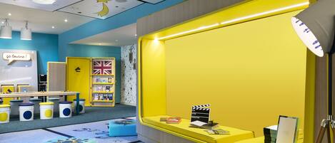 Un área de juegos infantil de colores vivos con una pared amarilla, un techo blanco decorado con estrellas y una alfombra azul con estampados de animales.