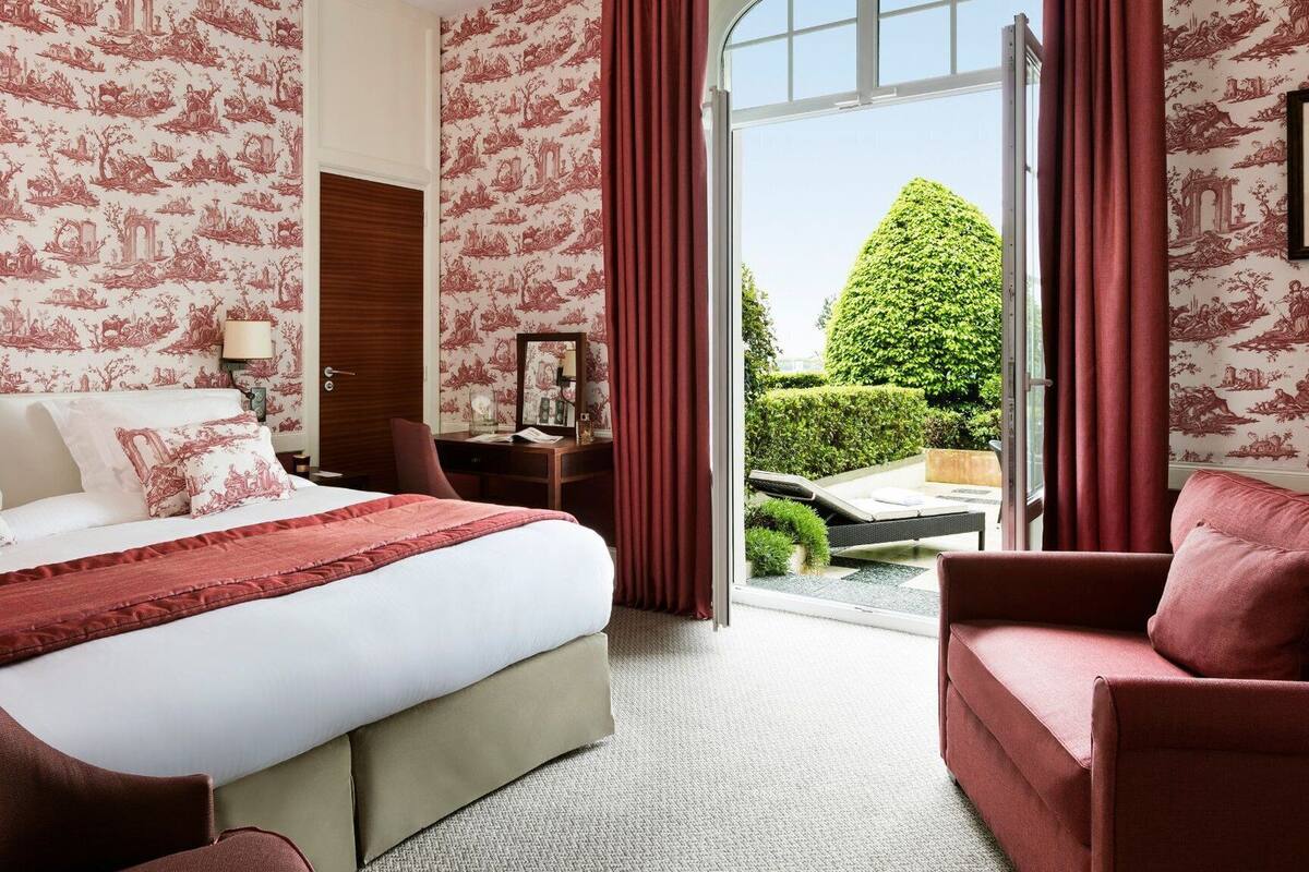 A hotel room with a large bed, a desk, and a view of a well-manicured garden.