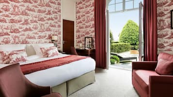 A hotel room with a large bed, a desk, and a view of a well-manicured garden.